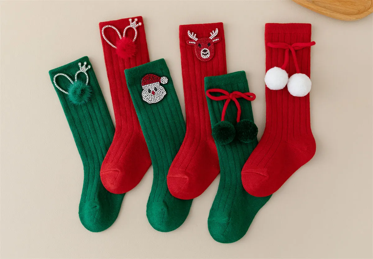 Close-up of red baby socks featuring a rhinestone crown and fluffy pom pom detail. Close-up of red baby socks featuring a rhinestone crown and fluffy pom pom detail.